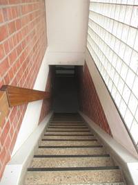gerade Treppe nach unten,  mit Handlauf links, links auch Backsteinmauer, rechts Wand aus Glassteinblöcken