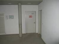 einflügelige Tür mit roten Schild, links davon Säule und Fluchtplan an der Wand 
