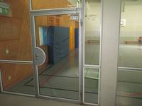 einflügelige gläserne Tür, in einer Glaswand, dahinter die turnhalle