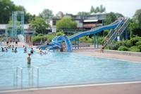 Großes schwimmbecken mit einer großen blauen rutsche und einer kleinen Kinderrutsche die ins Becken führt.