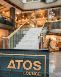 gerade Treppe mit Handläufen rechts und links führt ab Foyer mit Ladengeschäften eine Etage  aufwärts zur offenen Galerie mit Atos-Lounge