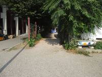 geschotterter Weg führt links am Gebäude der breidenbach studios vorbei, links vor dem Gebäude steht eine alte bemalte Badewanne. Links daneben befindet sich durch einen Zaun abgetrennt das Media-Markt-Gebäude