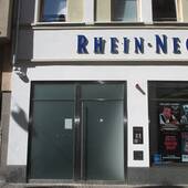 In einem mehrstöckigen Gebäude ist unten links Ein zweiflügelige Glastüre. Darüber beginnt der blaue Schriftzug der Rhein Neckr Zeitung 