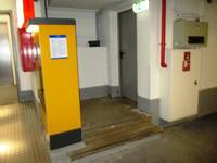 Einflügelige metallische Eingangstür, an einem Podest, vor dem Podest 2 Stufen an der anderen Seite des Podests ein Kassenautomat