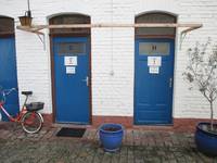 Blaue Toilettentüren, jeweils für Damen und Herren in einem weißen Gebäude im Hinterhof