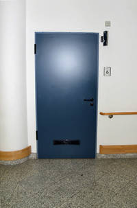 blaue Tür, rechts daneben Handlauf, davor Bodenbelag aus Fliesen