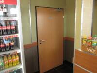 Braune Holztür in einer hellgrünen Wand. Rechts davon ein Teil der Theke, links Kühlschrank mit Getränken
