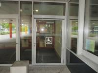 Glasfront, darin einflügelige Glastür mit Rollstuhlfahrersymbol