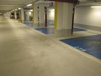 Tiefgarage, Parkplätze sind auf dem hellgrauen Betonboden blau eingezeichnet und mit Rollstuhlsymbol auf dem Boden versehen. Sie sind senkrecht zur Wand, Betonpfeiler trennen einige Parkplätze voneinander