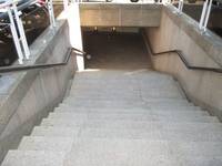 Eine abwärtsführende Treppe mit Podest und Handlauf links und rechts. Am Treppenende beginnt die Unterführung