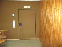 Eine Tür aus dem gleichen Material wie die Hallenwand mit Türgriff. Über der Tür grünes Leuchtschildnks