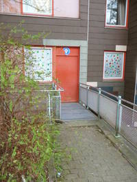einflüglige rote Tür, davor kleiner Steg mit Rillenplatten, linhs und rechts Geländer