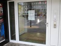 Breite einflügelige Glastür in einem hellen Rahmen, in der Tür hängen zwei Aushänge, rechts von der Tür ist eine Klingel zum Müller 