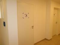 weiße Tür in weißer Wand, auf der Tür ist ein Schild angebracht. Rechts daneben eine weitere Tür