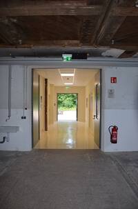 offen stehende Raumhohe Tür, dahinter offener Vorraum/Flur. Links und rechts gehen Türen zu Toiletten ab, geradeaus offen stehende Tür zu Außengelände/Bauernhofbereich
