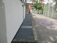 Rampe aus Metall mit seitlicher Zufahrt, endet auf Podest, links davon Zufahrt aus Betonverbundsteinen, darauf Straßenschild parken verboten gemalt