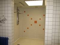 Duschbereich mit einem sichtbaren Duschplatz, der Raum ist weiß gekachelt, etwa in der Mitte ist ein orangens \\