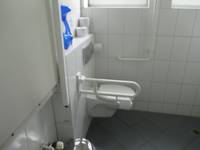 Weiße Toilette mit Haltegriff an einer weiß gekachelten Wand