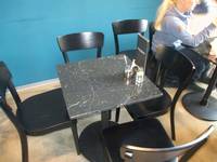  eckiger Bistrotisch mit vier Stühlen, auf dem Tisch eine Speisekarte und ein Salzstreuer