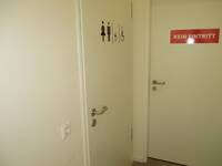 Eine weiße Türe in einer weißen Wand. Auf der Tür Symbole für Mann, Frau, Rollstuhlnutzende und Wickeltisch