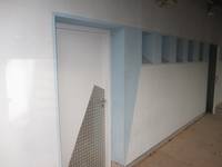 eiflügelige weiße Tür mit einem hellblauen Rahmen. Unten ein diagonalverlaufender Metallbeschlag, rechts von der Tür in Kopfhöhe blau umrandete Öffnungen