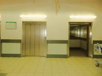 2 Aufzüge nebeneinander in gefliesten Eingangsbereich, auf Griffhöhe links und rechts neben Aufzügen sind Bretter angebracht