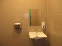 Ein weißes Waschbecken an einer hellbraun gekachelten Wand. Über dem Waschbecken hängt ein rechteckiger Spiegel