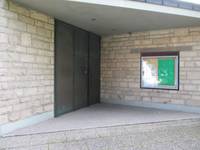 Eingang mit dreiflügiger Drehflügeltür, rechts der Tür an der Wand ist Informationstafel