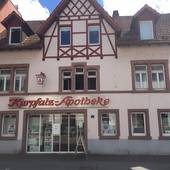 Historisches Gebäude mit hohem Giebel, im EG breite Schaufensterfront. Über dem Schaufenster ist der Schriftzug "Kurpfalz-Apotheke" angebracht
