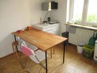 Ein Raum mit einem hellen Naturholztisch, 2 weißen Klappstühlen und 2 Holzhockern.