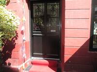 Eine braune Metalltür mit 4 eingelassenen Scheiben im oberen Bereich. Die Tür ist in der roten Sandsteinfassade etwas zurückversetzt. 