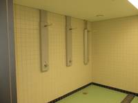weiß gekachelter Raum mit drei Duschplätzen, Bodenbelag ist grün gefliest