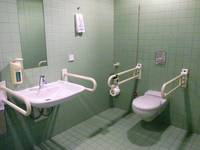 gekachelter Raum, darin Toilette mit Haltegriffen und Waschbecken mit Haltegriffen
