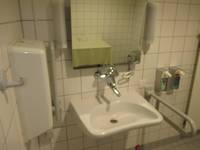 Waschbecken mit einem Haltegrifff rechts und links. Spiegel, Seifenspender und Handtuchhalter vorhanden