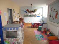 Raum mit einem Spielehaus, mit Spielmatten, einem Kindertisch mit Stühlen, einem Sessel und diversen Spielsachen, die Wände sind bemalt oder es hängen Kinderbilder daran