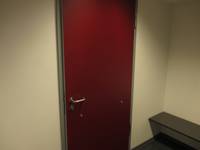 rote Tür vor hellen Wand, rechts davon ein Stück der Umkleidebank