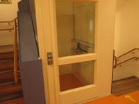 Geschlossene Glastür mit breitem weißen Rahmen, dahinter Aufzug-Kabine
