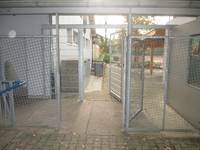 zwei offenstehende Gittertore hintereinander im Abstand von wenigen Meter, rechts und links setzen sich die Tore in Zäune fort
