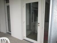Ein Glastür in einem weißen Rahmen, davor offene Terrasse mit Gartenstühlen
