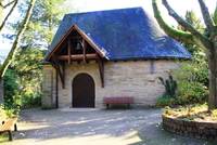 Kapelle aus Naturstein mit schwarzem Dach, über Eingang kleines Vordach mit Glocke, Weg aus Pflastersteinen mit 2 Bänken